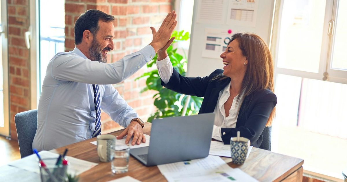 Two colleagues high-fiving across a desk in a bright office